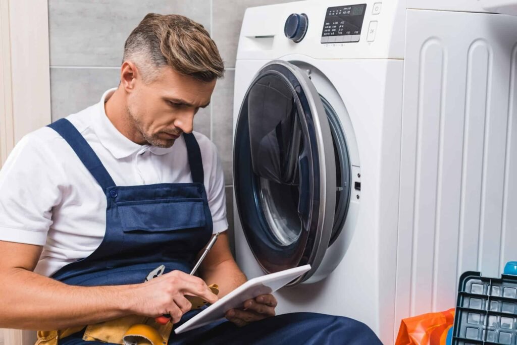 Technician repairing a washing machine while using a digital tablet